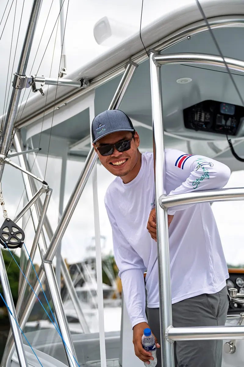 Tripulante sonriendo a bordo, con gorra y camisa de pesca blanca