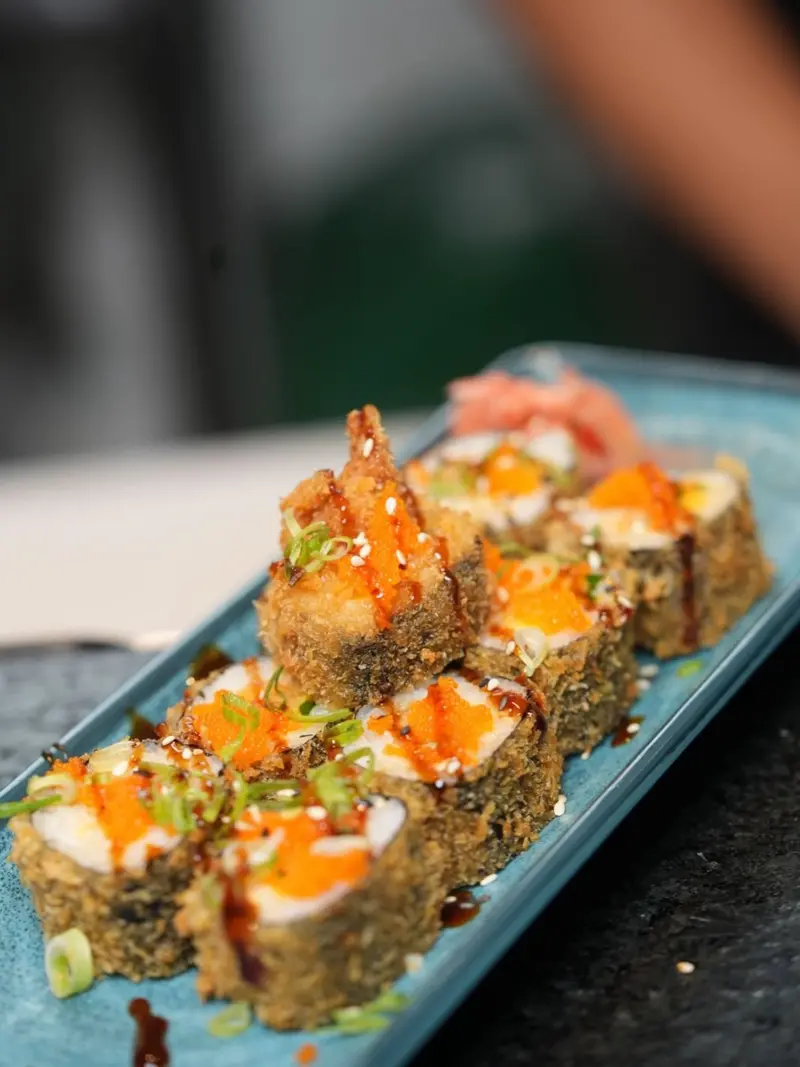 Tempura Ebi Roll con masago naranja, salsa unagi y cebollín, en una bandeja turquesa