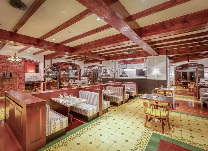 Salón con mesas puestas, bancos a rayas, piso de mosaico y techo de vigas de madera