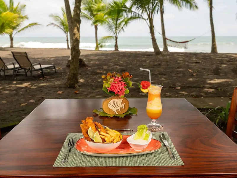 Plato de frituras con salsas y un jugo de fruta en una mesa con la playa de fondo