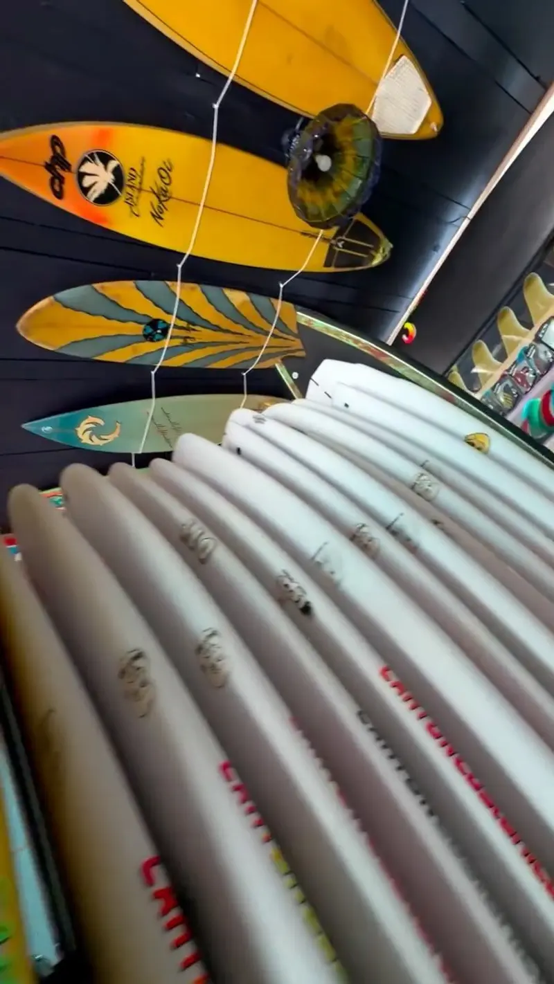 Pila de tablas de surf blancas bajo tablas colgadas del techo del taller