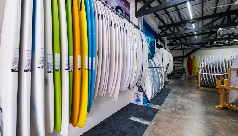 Pasillo de la tienda con tablas de surf de colores en estantes de ambos lados y accesorios al fondo