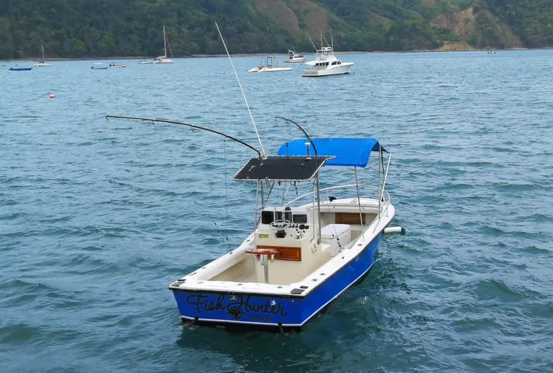 El barco azul con toldo y dos cañas de pesca fondeado frente a la bahía