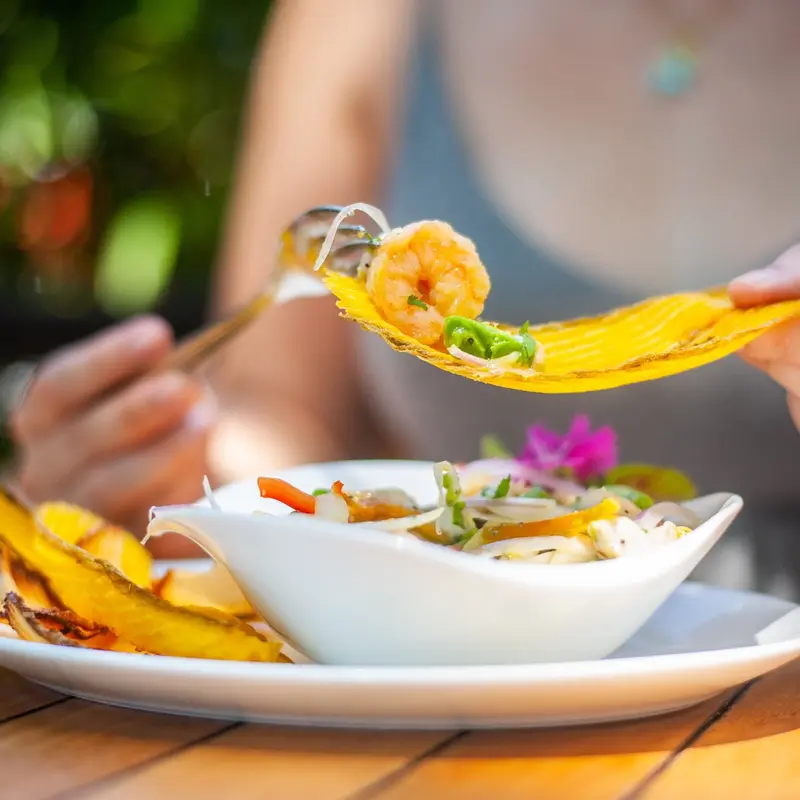 Bol de ceviche con chips de plátano y un tenedor con pasta y camarón en primer plano