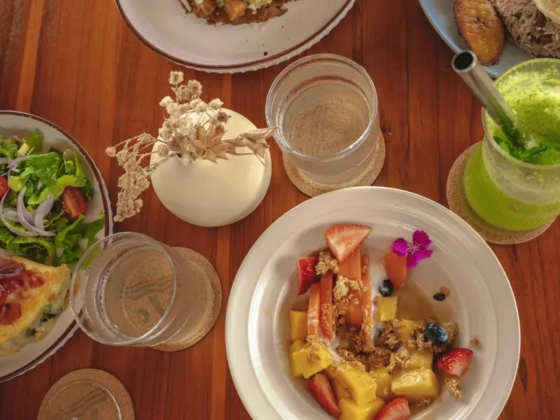 Mesa con desayuno: fruta, ensalada, jugo verde y platos servidos sobre madera