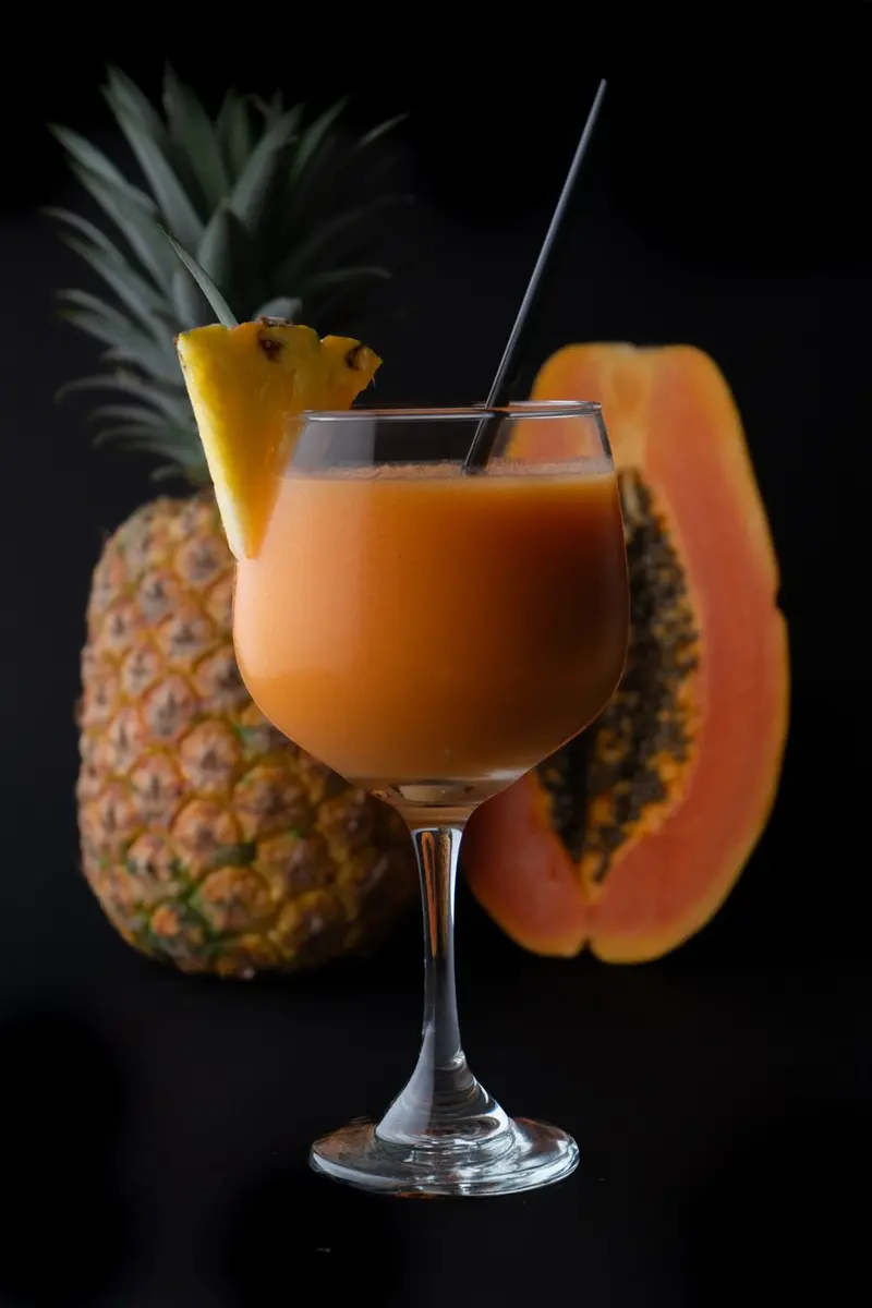 Batido de papaya y piña en copa, junto a una piña y una papaya partida
