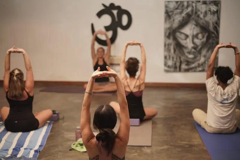 Clase de yoga en el estudio: alumnos sentados con los brazos extendidos sobre la cabeza