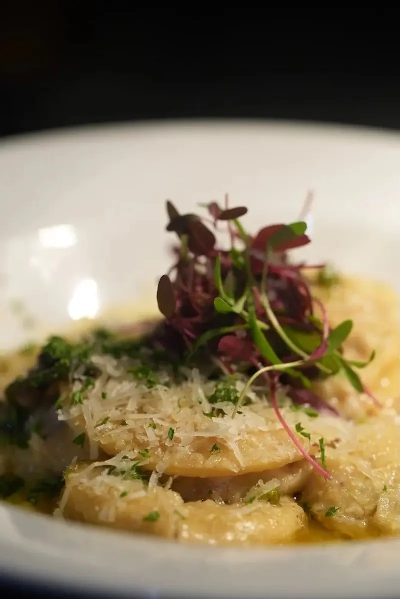 Pasta rellena con queso rallado y brotes morados en un plato blanco