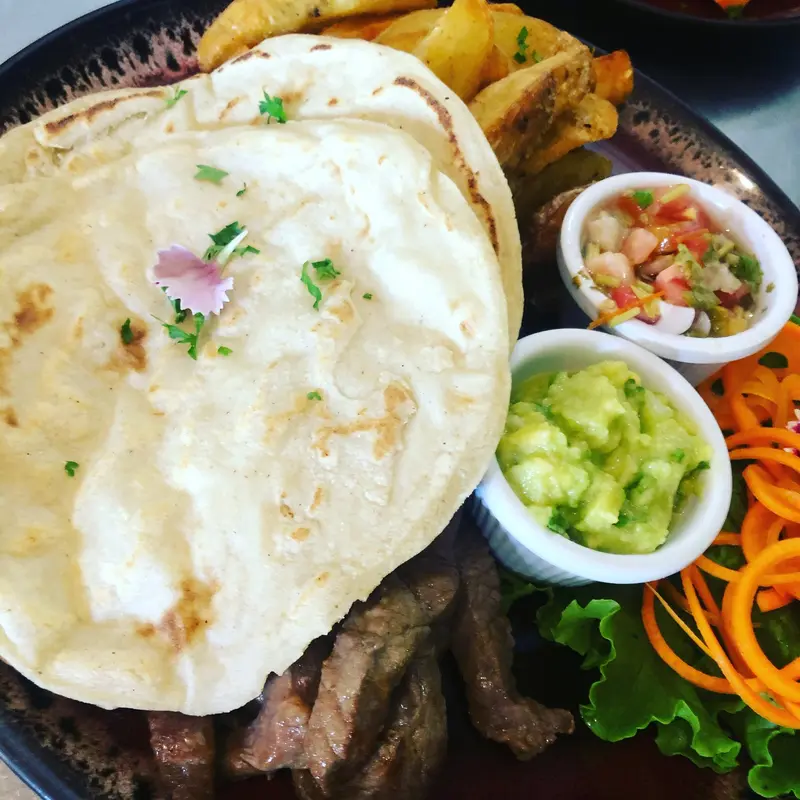 Plato con tortillas, carne a la parrilla y cuencos pequeños de guacamole y pico de gallo