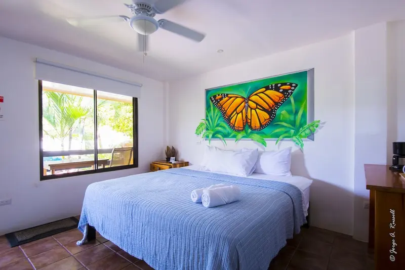 Habitación con cama azul, ventana y un mural de una mariposa monarca en la pared