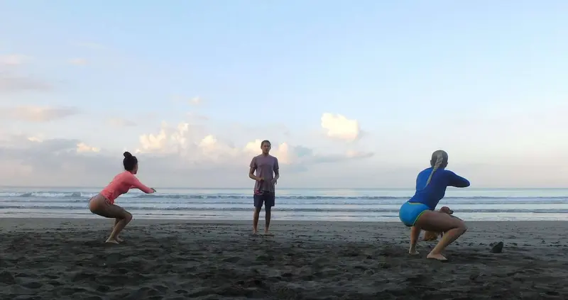 Tres personas practicando en la arena oscura de la playa bajo un cielo con nubes