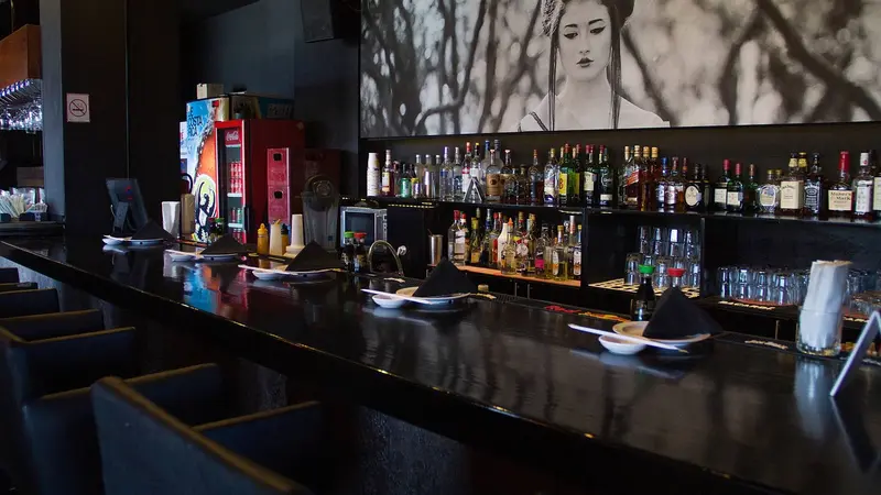 Barra del restaurante con botellas en la pared y un mural de una geisha