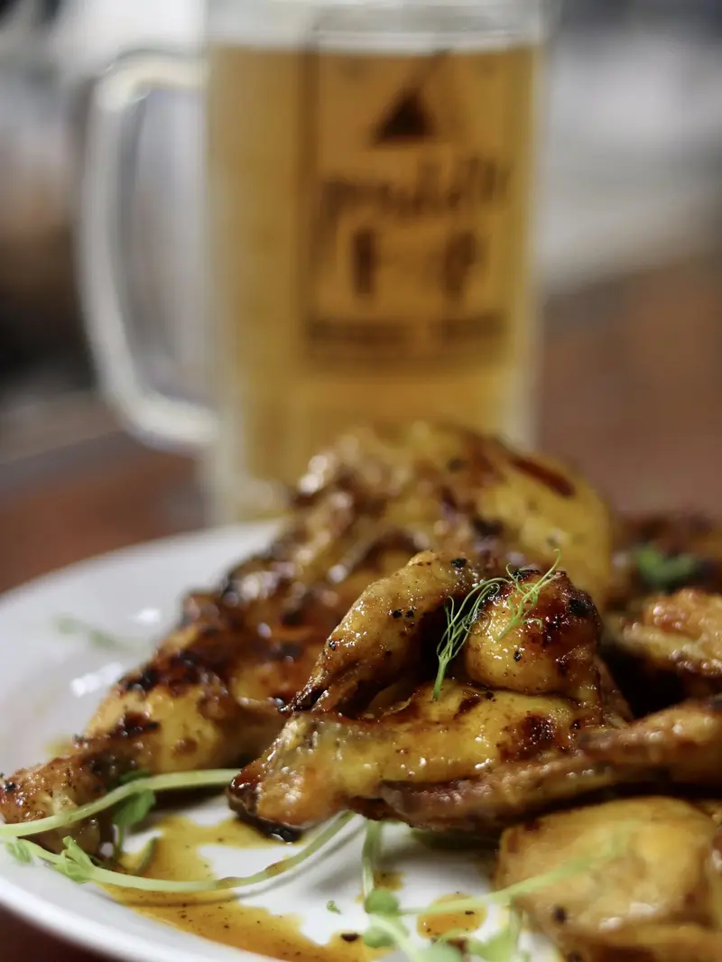 Alitas de pollo glaseadas en un plato con una jarra de cerveza al fondo