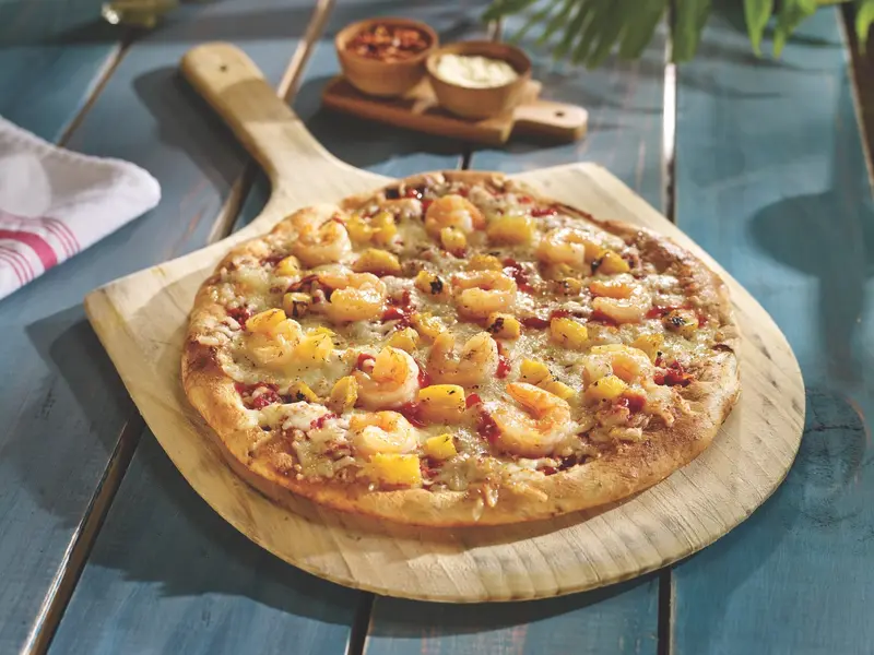 Pizza con camarones y piña sobre una tabla de madera, con dos salsas al fondo