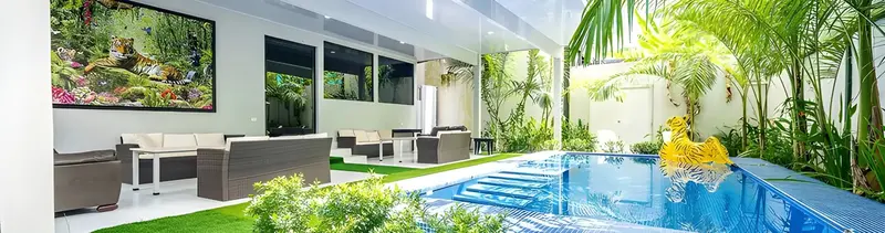 Sala exterior con sofás, un cuadro de tigre y una piscina rodeada de jardín