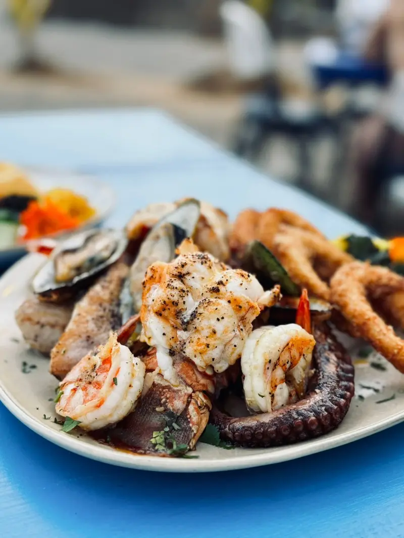 Plato de mariscos con langosta, camarones, pulpo, mejillones y aros de calamar sobre una mesa azul