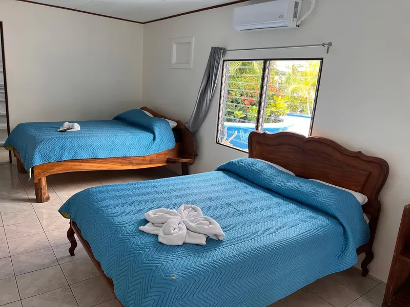 Habitación con dos camas matrimoniales de colcha azul junto a la ventana