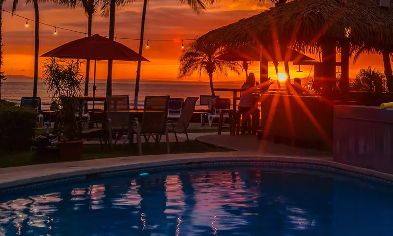 Atardecer naranja entre las palmeras sobre las mesas del tiki bar y la piscina