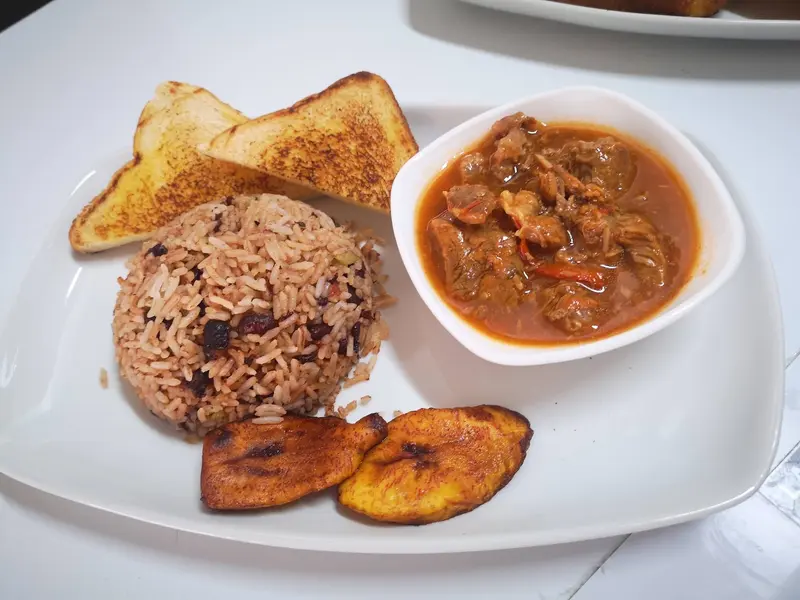 Gallo pinto con carne en salsa, plátano maduro frito y pan tostado en un plato blanco