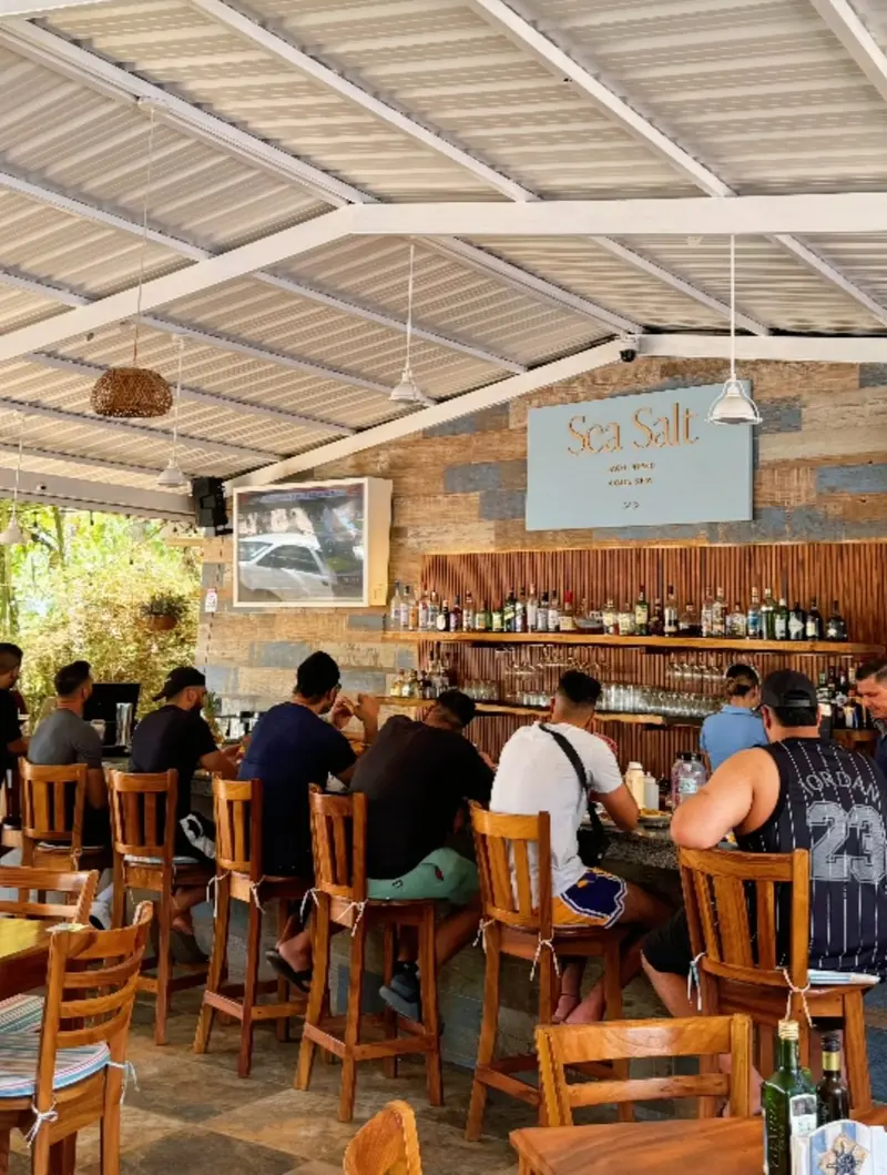 Barra del restaurante con bancos de madera, botellas detrás y un techo blanco con vigas