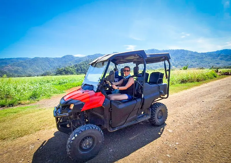 Buggy rojo con una conductora en un camino de tierra, con campos y montañas al fondo