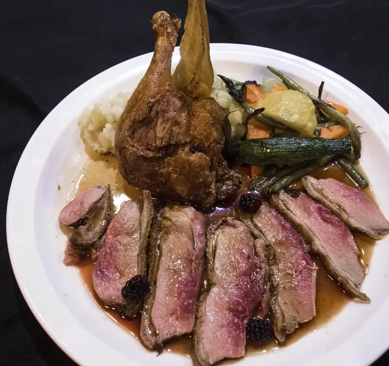 Pato asado con rebanadas de pechuga y vegetales sobre un plato oscuro