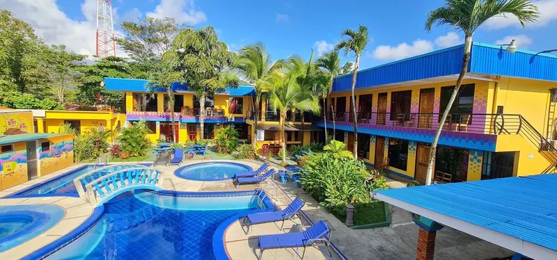 Edificio de dos pisos de colores y piscinas vistos desde arriba, con palmeras alrededor