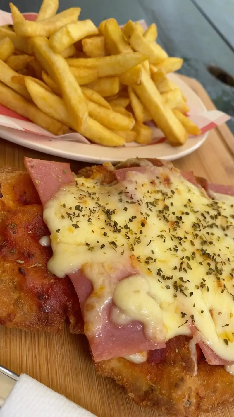 Milanesa con jamón y queso gratinado y papas fritas sobre una tabla de madera