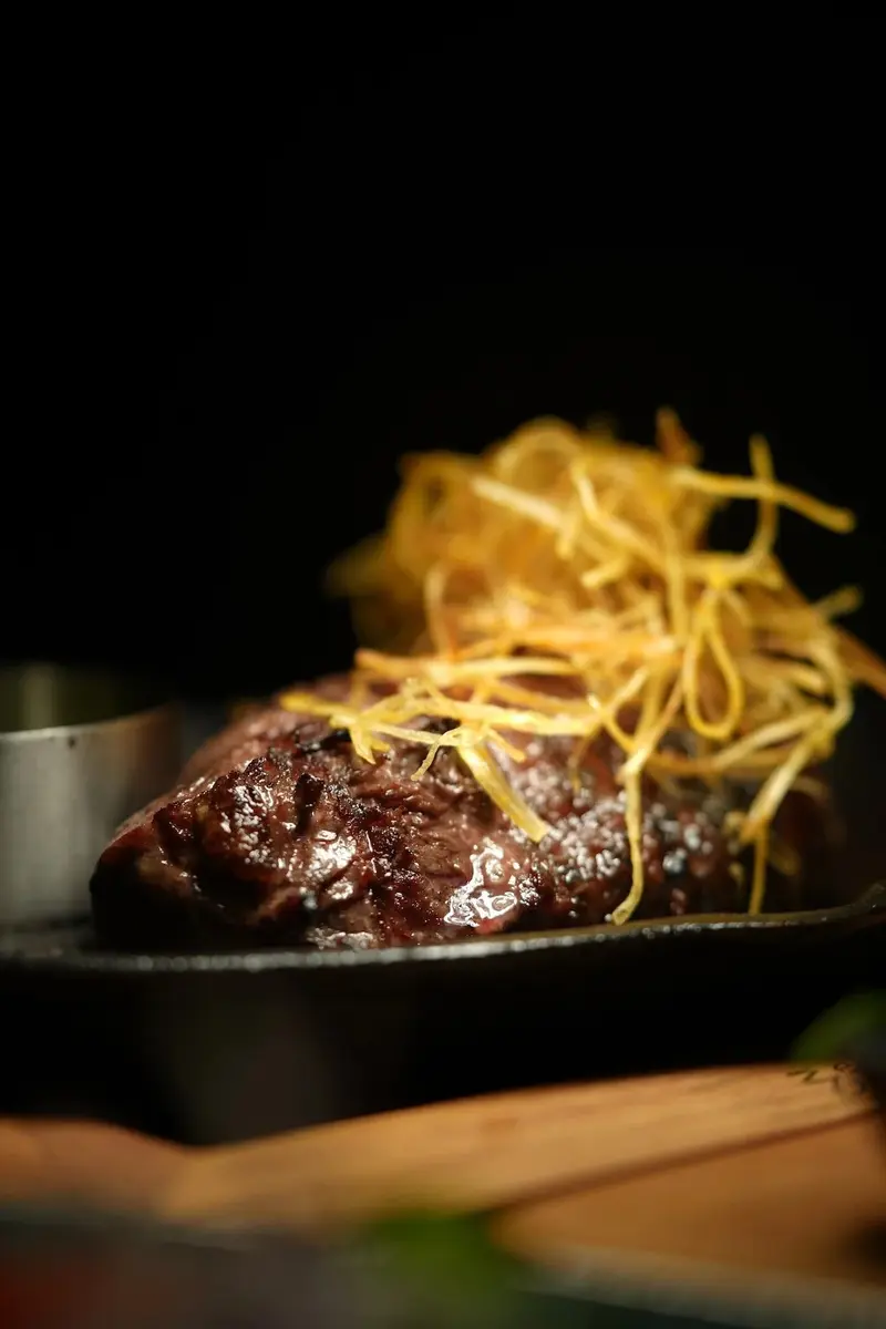 Corte de carne en una sartén de hierro, coronado con papas crujientes en hilos