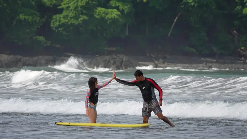 Instructor y alumna se chocan las manos en el agua, con una tabla amarilla flotando detrás