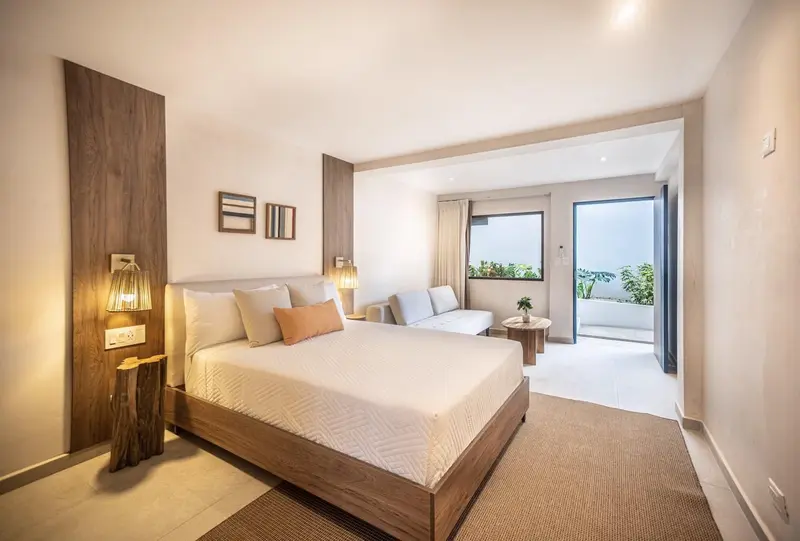 Habitación con cama queen de cabecera de madera, sofá y puerta corrediza al balcón