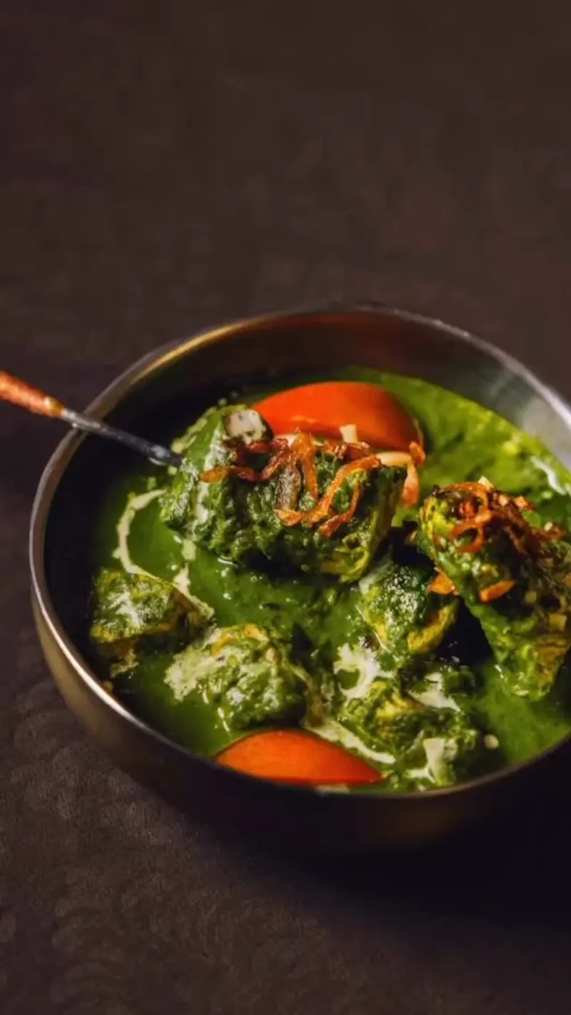 Espinacas cocidas con tomate en un cuenco oscuro, con una cuchara a un lado