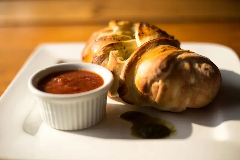 Panes de ajo horneados con un recipiente de salsa marinara sobre un plato blanco