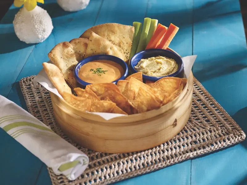 Canasta con pan plano, chips de tortilla y vegetales, con dos dips en cuencos azules