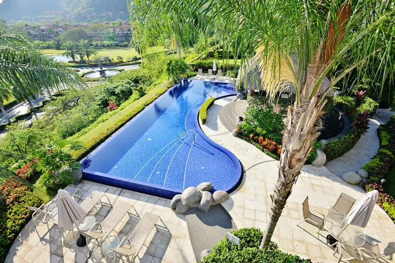 Vista aérea de una piscina de forma sinuosa rodeada de jardín y reposeras
