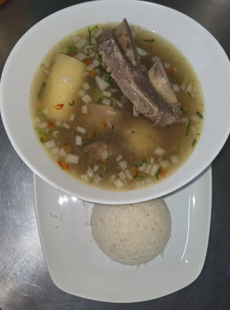 Sopa de carne con yuca y verduras en un plato hondo, con una porción de arroz blanco