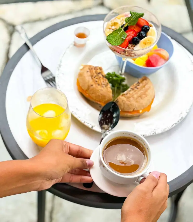 Desayuno con huevos, tostada, fruta, yogur con granola, jugo de naranja y té servido sobre una mesa blanca