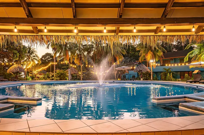 Piscina circular con fuente, iluminada al atardecer bajo un techo de palma