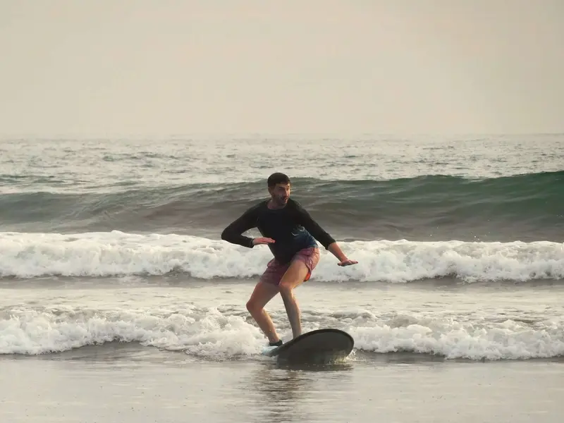 Surfista oscuro con tabla negra deslizándose sobre la espuma de una ola al atardecer