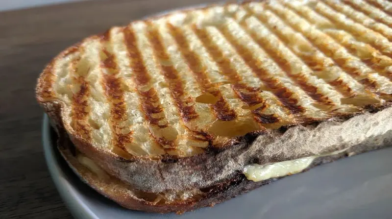 Sándwich prensado con marcas de plancha y queso derretido sobre un plato gris