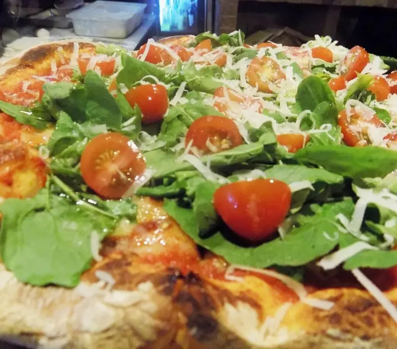 Pizza con rúcula, tomates cherry y queso rallado sobre masa de borde tostado