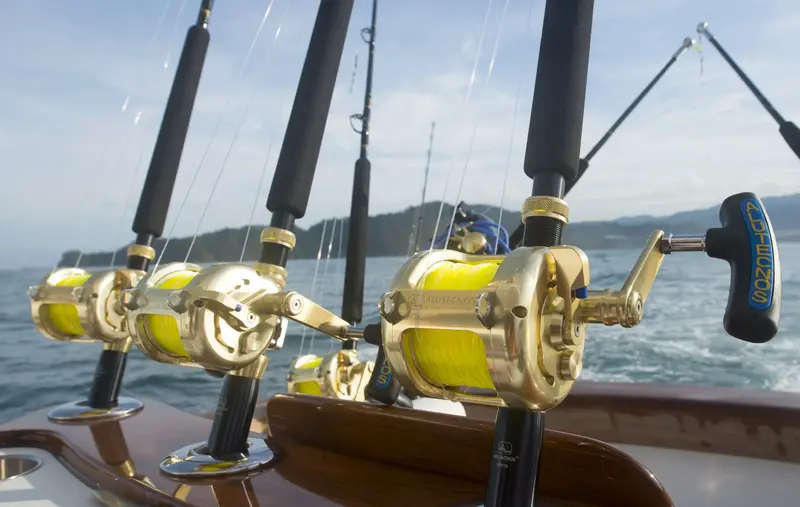 Tres carretes de pesca dorados montados en sus cañas sobre la borda de un barco