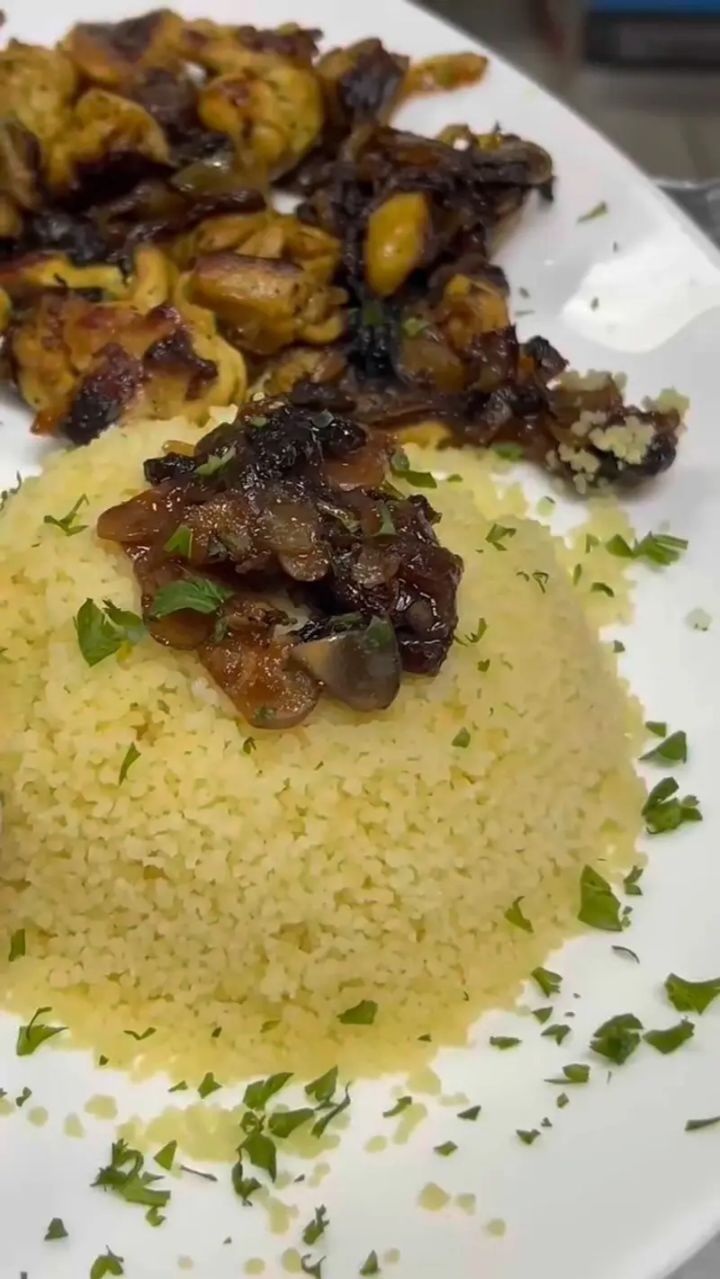 Montaña de cuscús amarillo con carne y vegetales salteados sobre un plato blanco