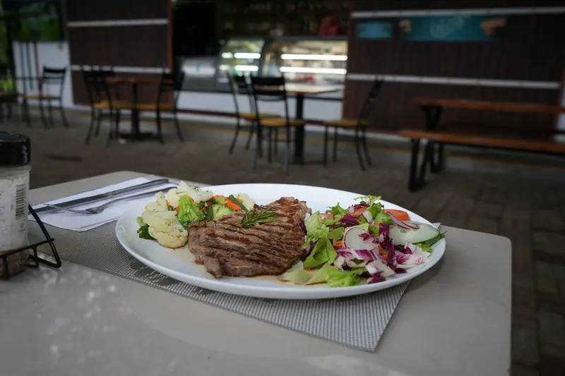 Filete a la parrilla con ensalada en un plato blanco sobre una mesa de la terraza