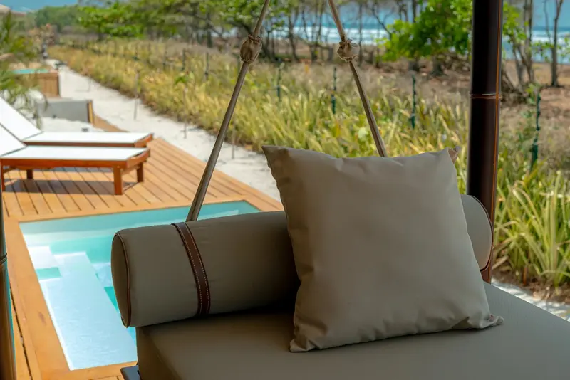 Hamaca-sofá junto a una piscina pequeña y reposeras frente a la playa