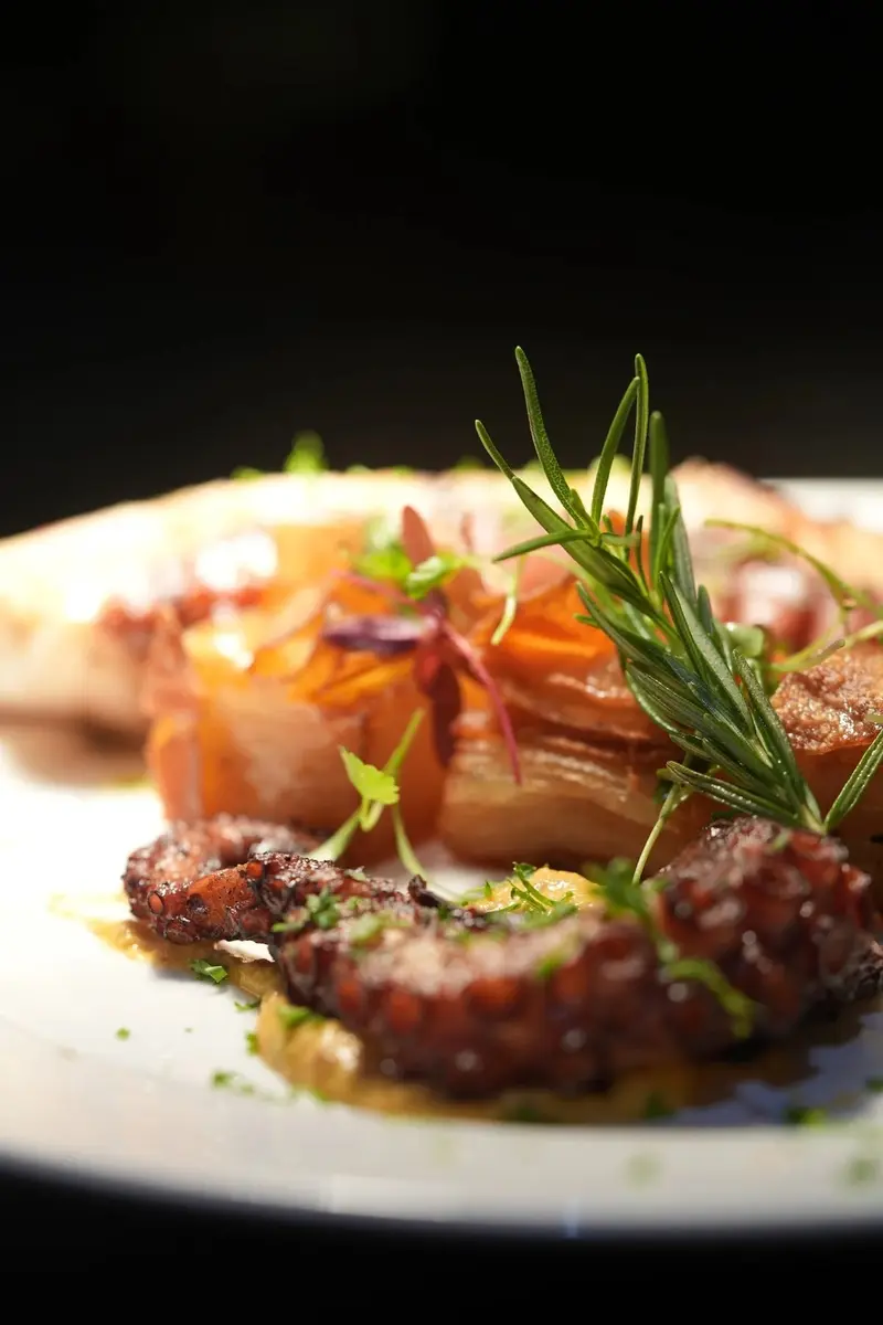 Pulpo a la parrilla con ramita de romero sobre un plato blanco