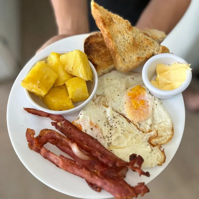 Plato de desayuno con huevos fritos, tocineta, tostada, piña y mantequilla