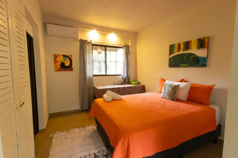 Habitación con cama de cubrecama naranja, ventana y aire acondicionado