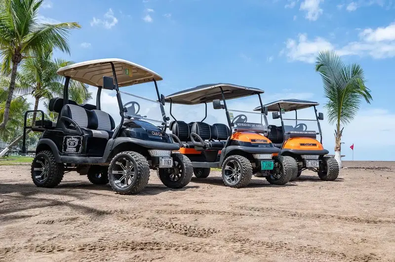 Carritos de golf naranjas y negros estacionados en fila sobre la arena de la playa de Jacó