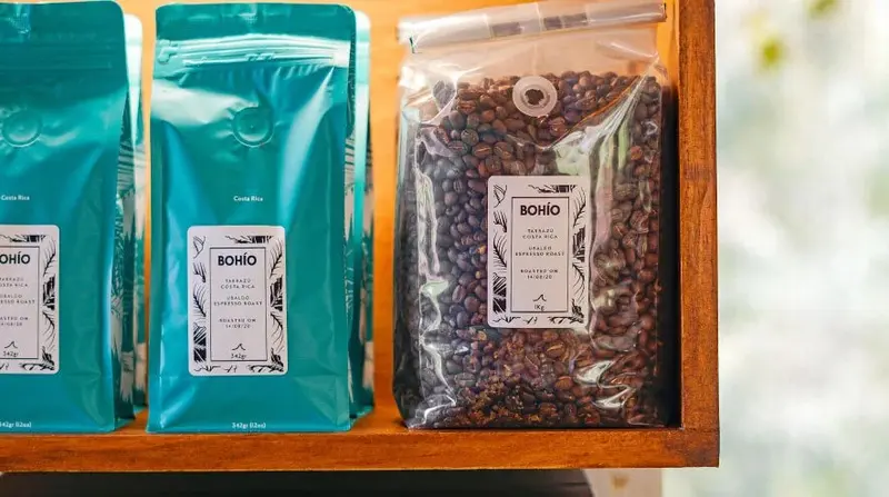 Bolsas de café turquesa y una de granos transparente en un estante de madera